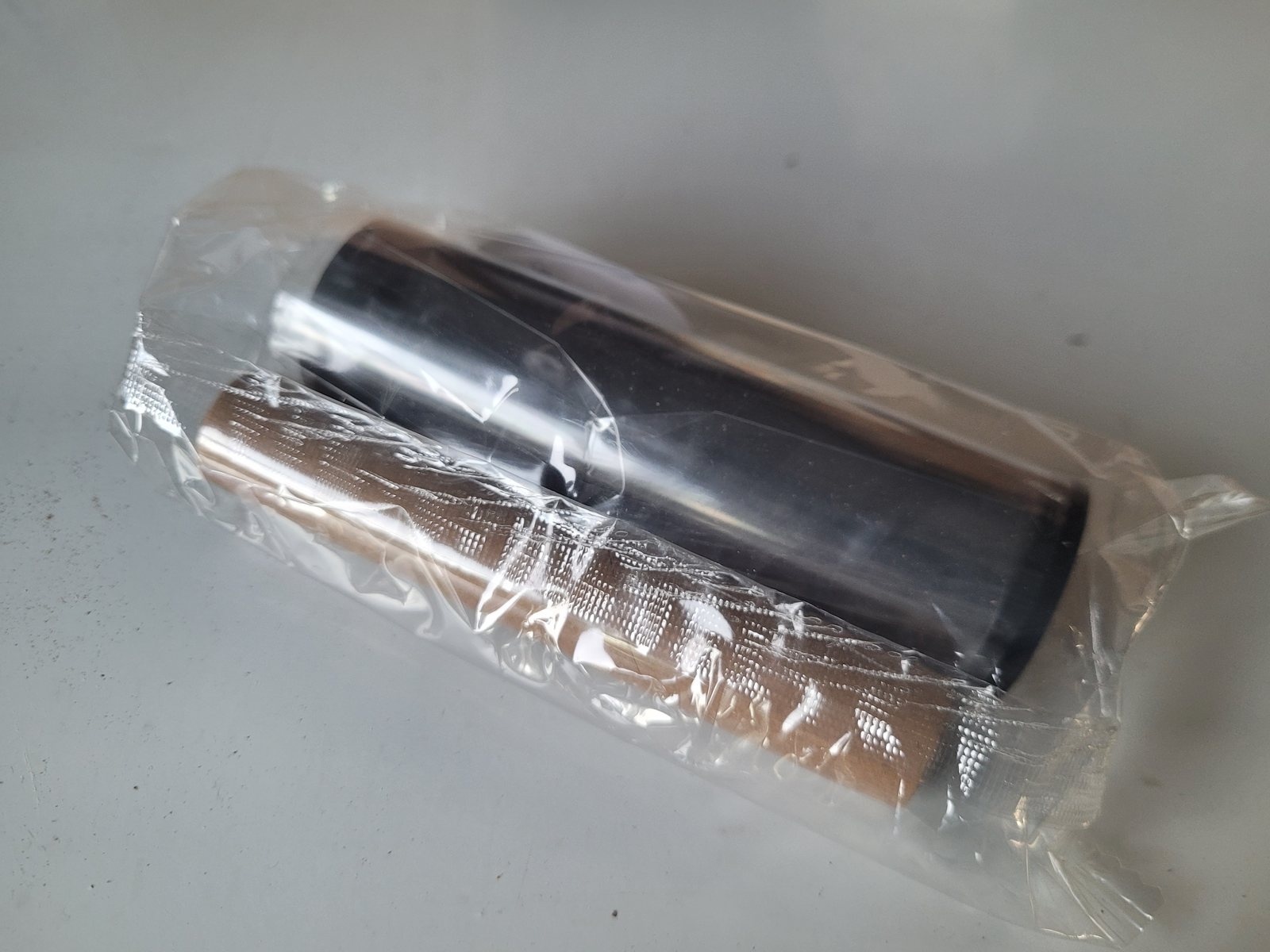 A desktop printer ribbon sealed in its bag, lying beside the empty cardboard
                  take-up core that comes with it